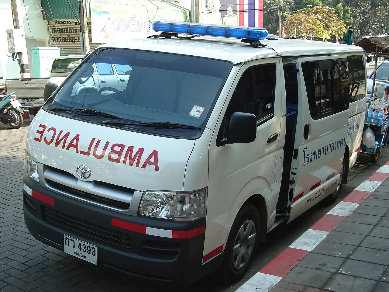 Front of a white ambulance van with the word AMBULANCE in mirror writing across the bonnet, parked in Chiang Mai.