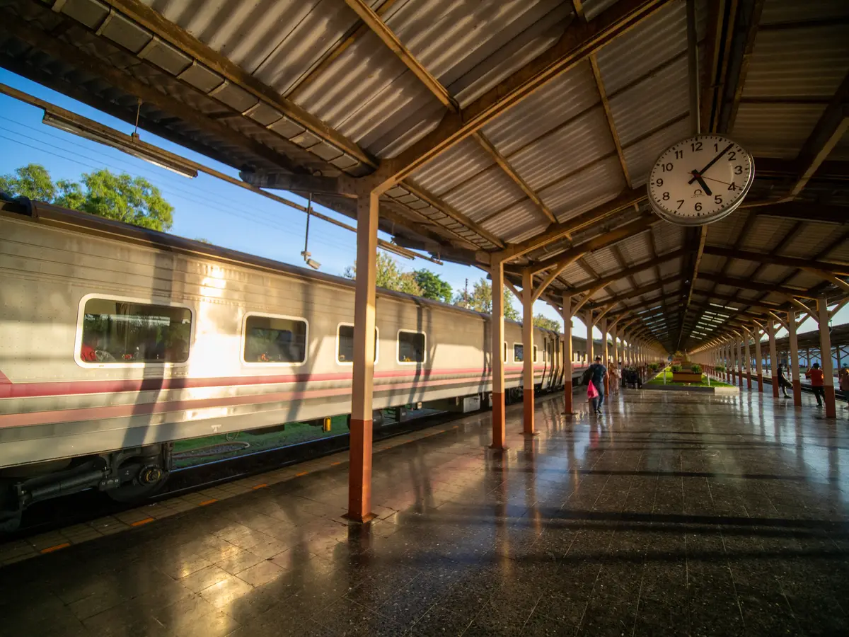 Passenger train standing beside a covered platform with a station clock and roof supports.