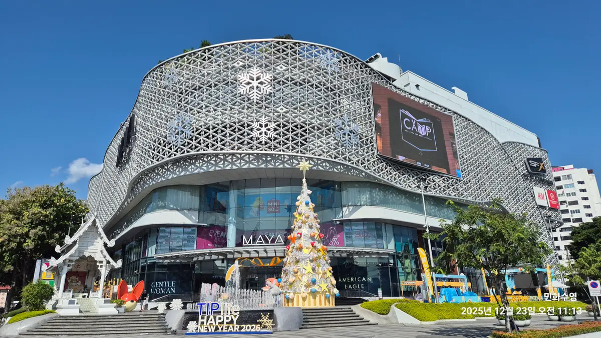 Lattice-patterned facade of the MAYA shopping centre with a decorated tree and a large screen at the entrance.