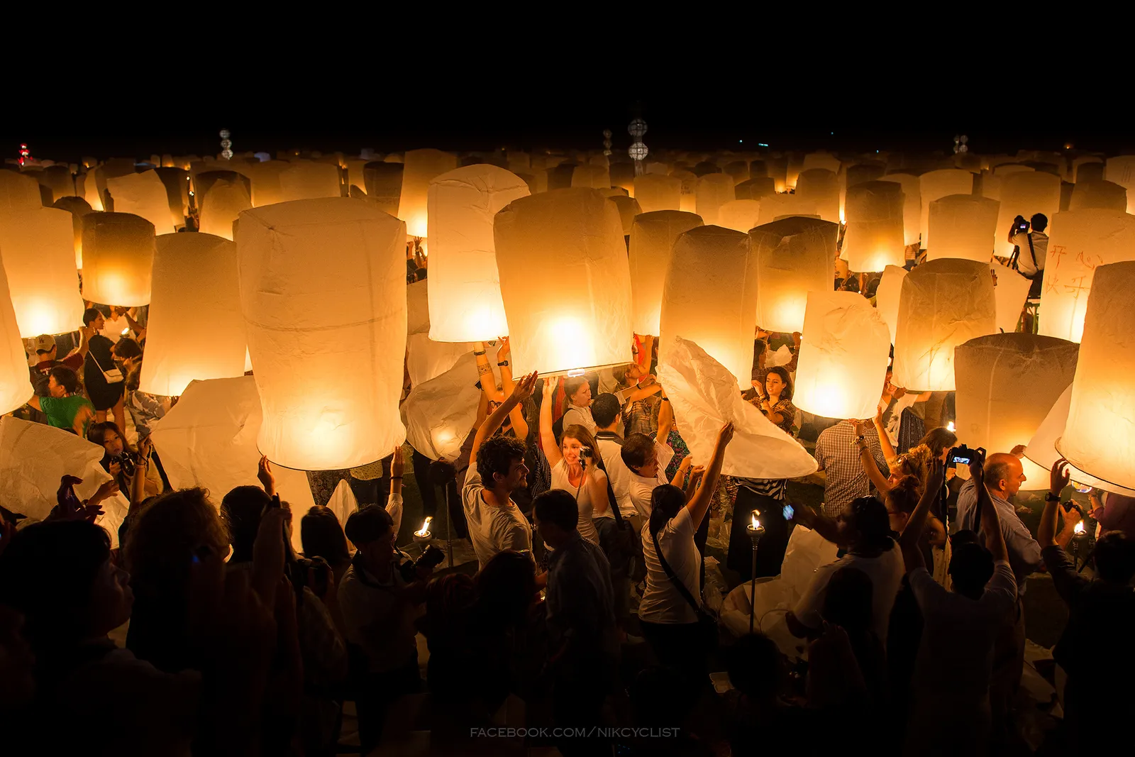 Crowd at night holding up large glowing paper lanterns just before release.