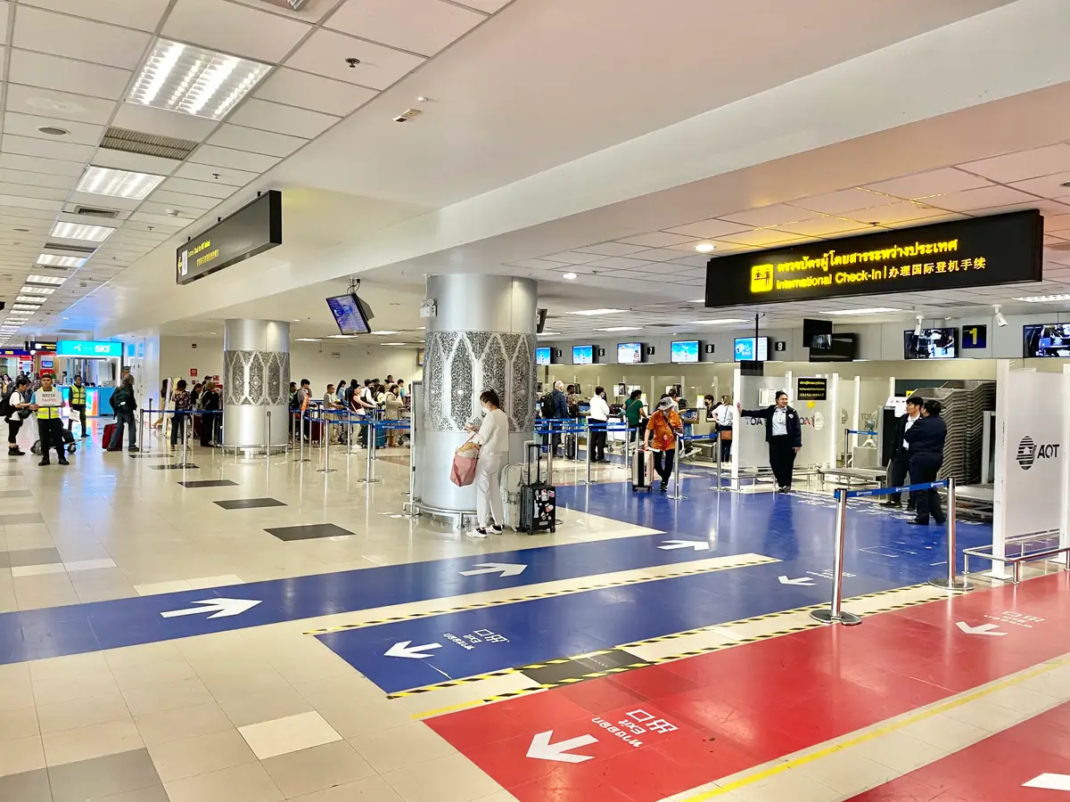 Airport hall with blue and red floor arrows and overhead direction signs.