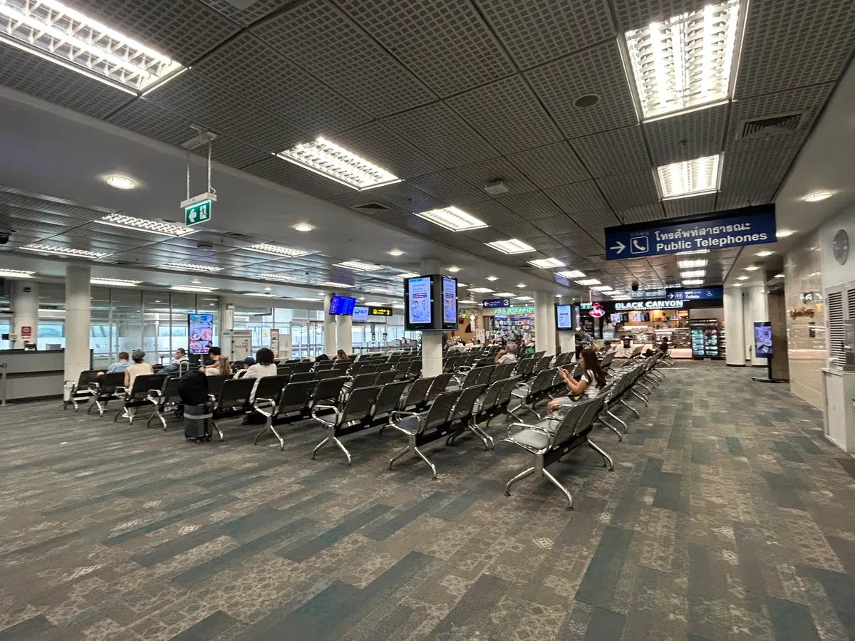 Waiting area with rows of grey seats and ceiling lights.