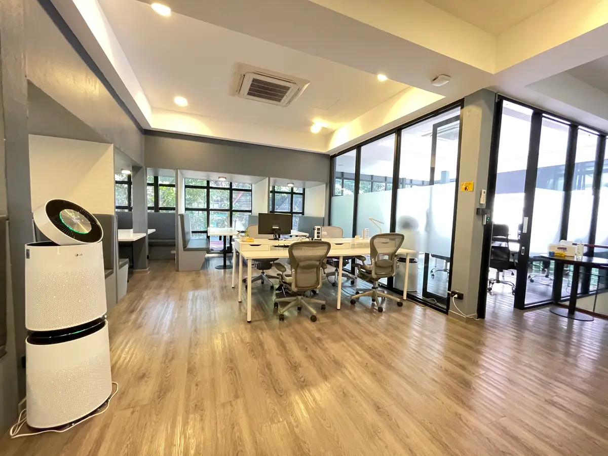 Wide room with wooden floor, a long meeting table, office chairs and tall windows.