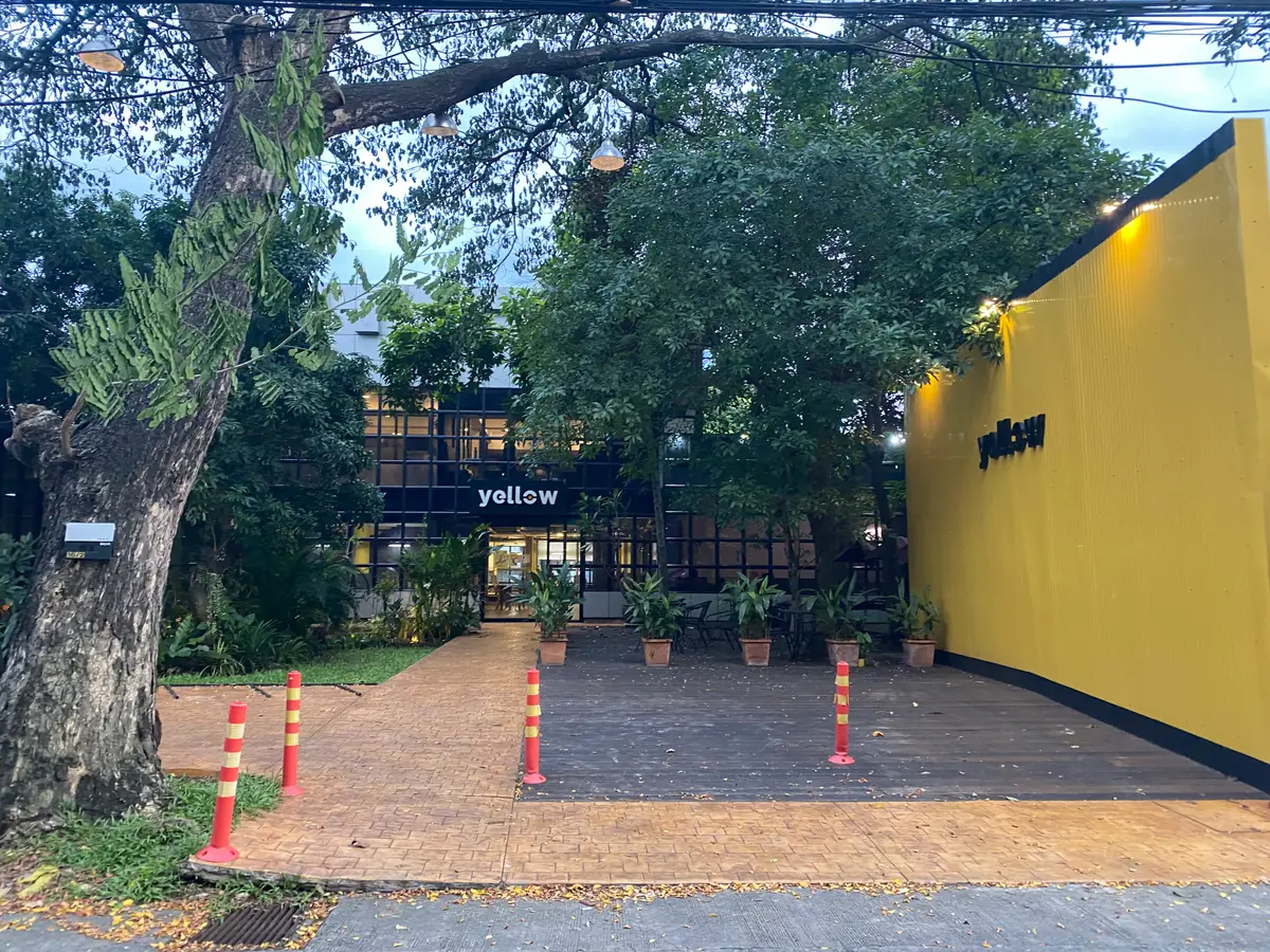 Brick path leading to a dark glass building with a yellow wall and a logo sign.