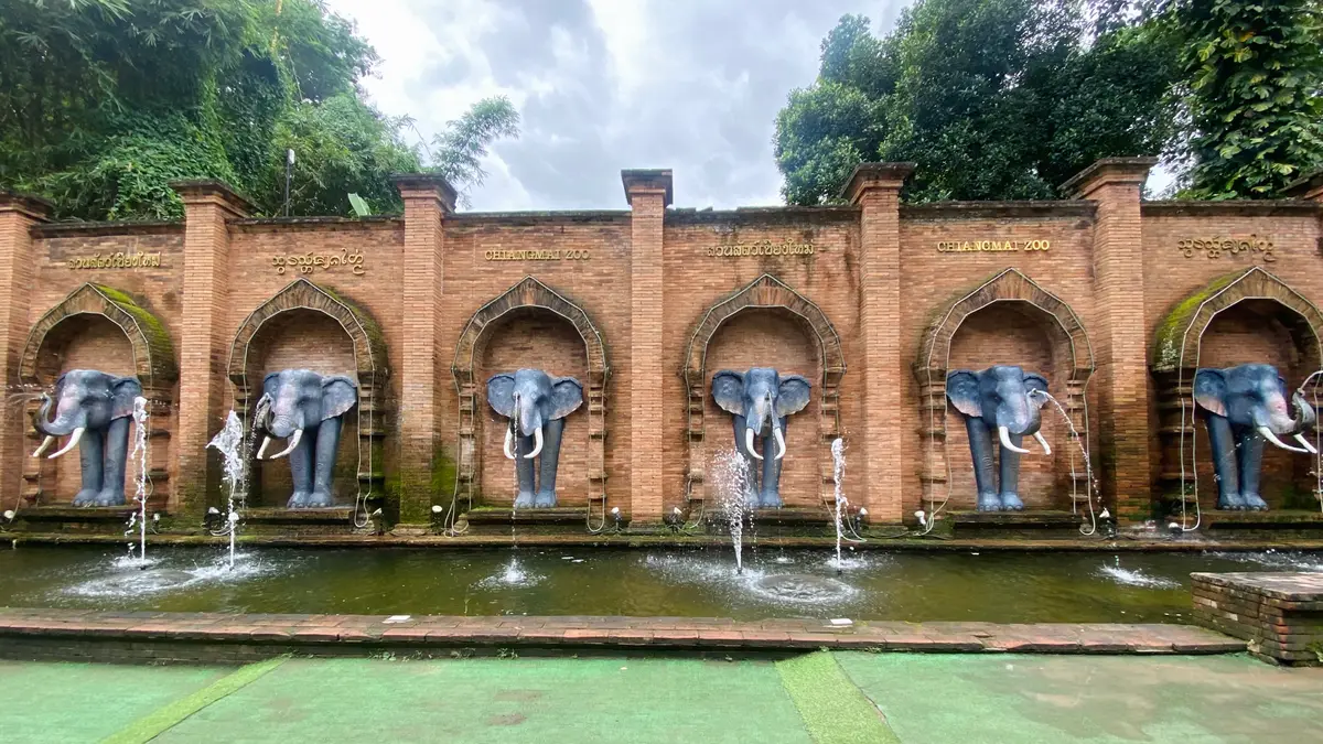 A brick wall with four arched niches, each holding a stone elephant head over a water spout.