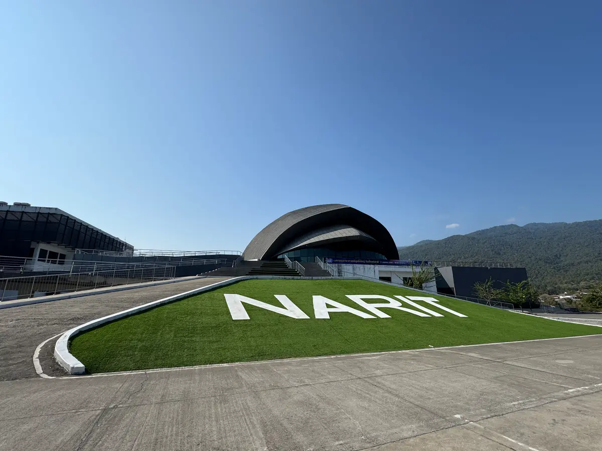 The curved roof of the planetarium behind a lawn with the NARIT name in white letters, mountains beyond.