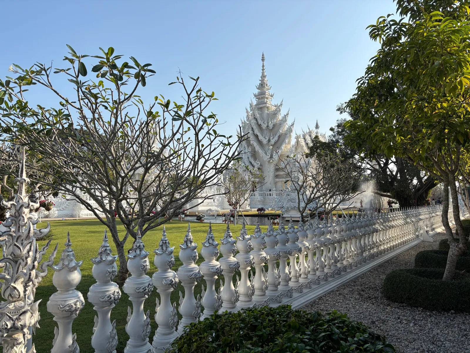 White stone railing leading toward a white spired shrine across a garden
