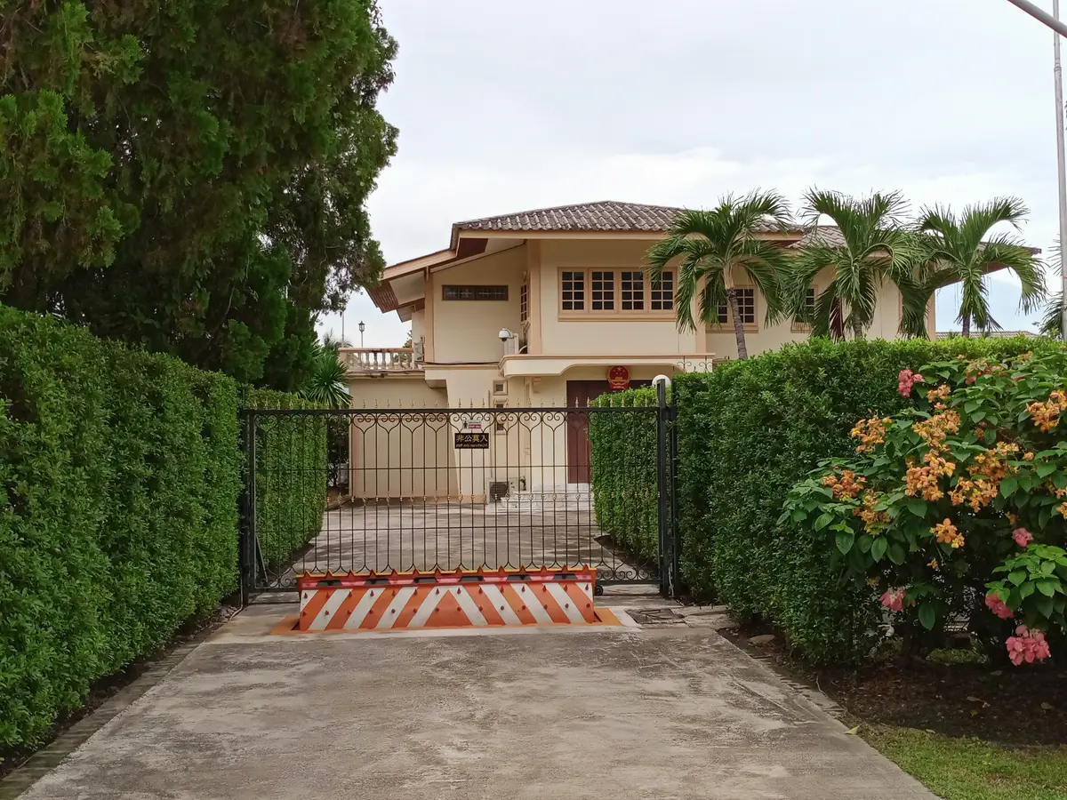Gate and a low building behind hedges and palm trees at the Chinese consulate