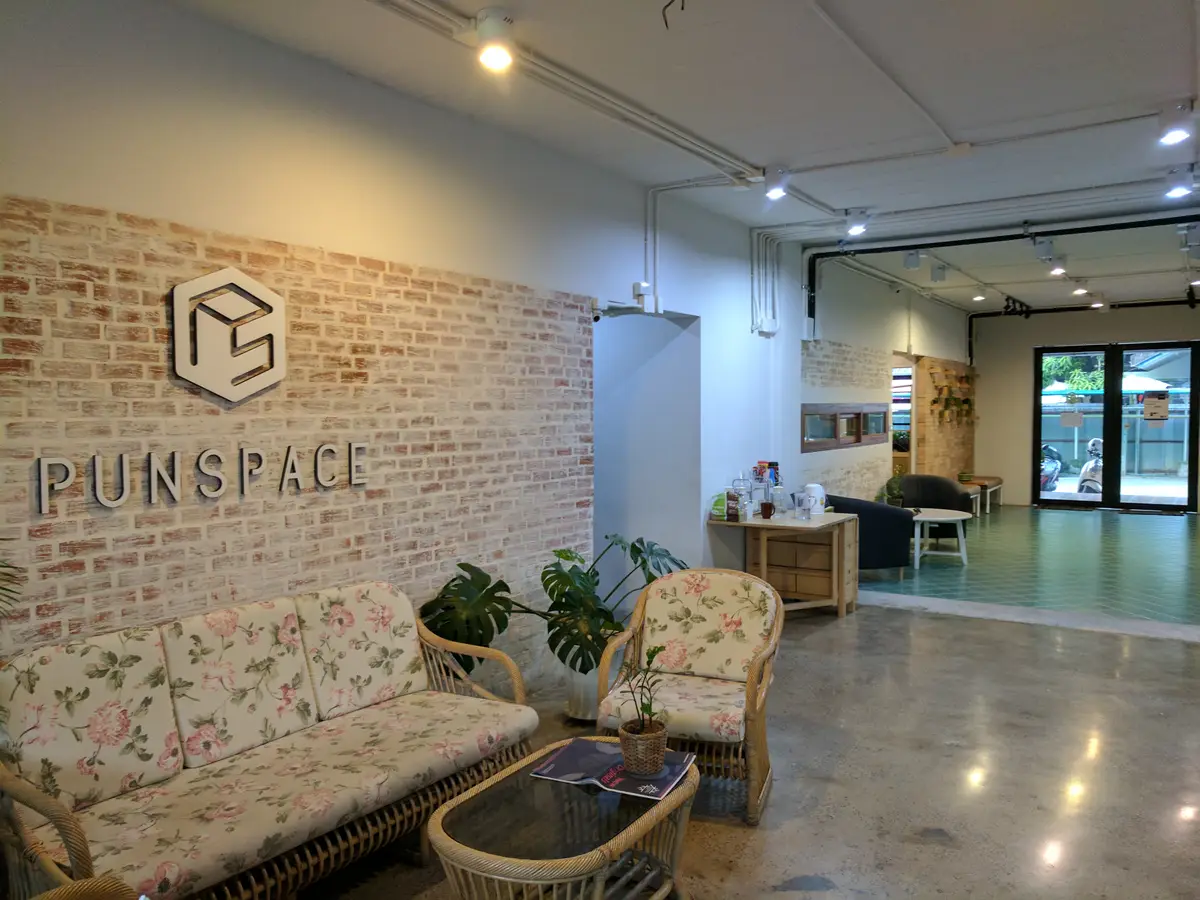 Reception corner with a brick wall, a wall logo and two patterned armchairs.