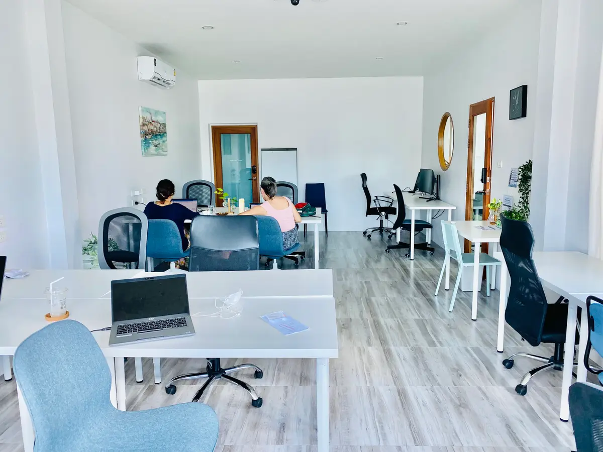 Bright room with white desks, blue chairs and two people working at laptops.