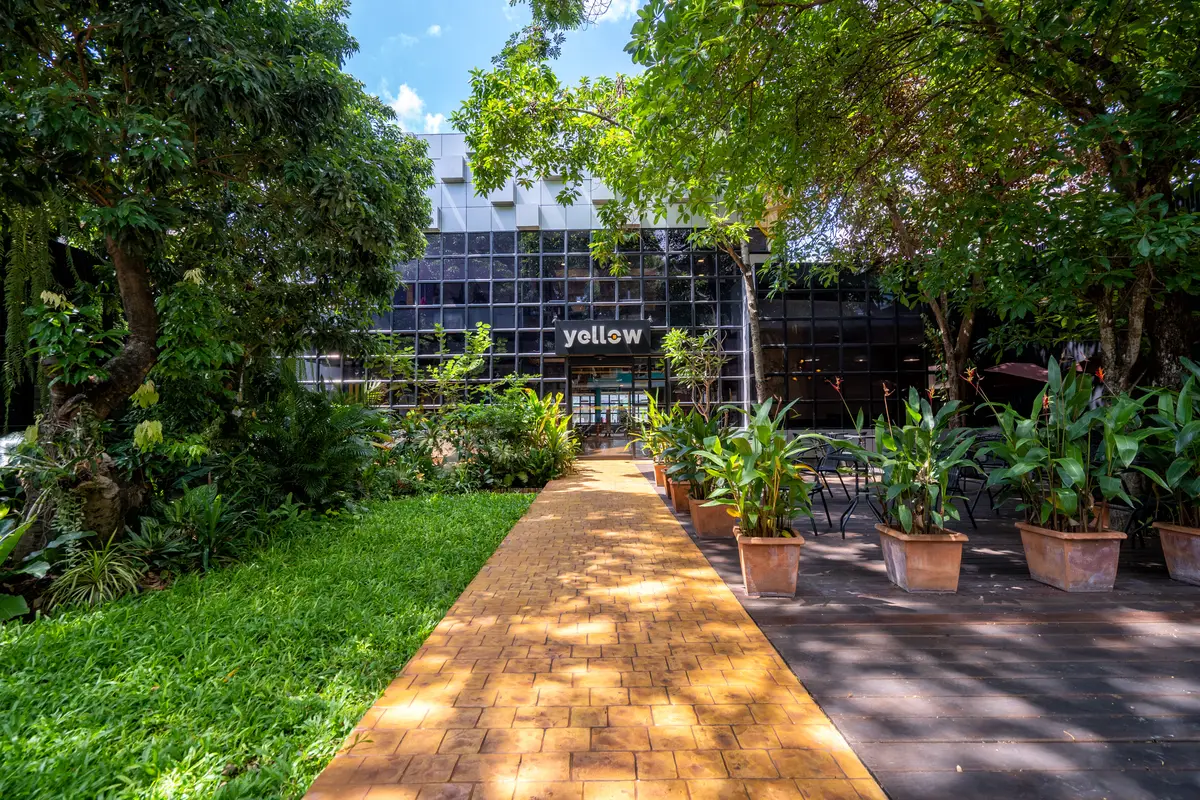 Brick path leading through a garden to a dark glass building with a yellow logo sign.