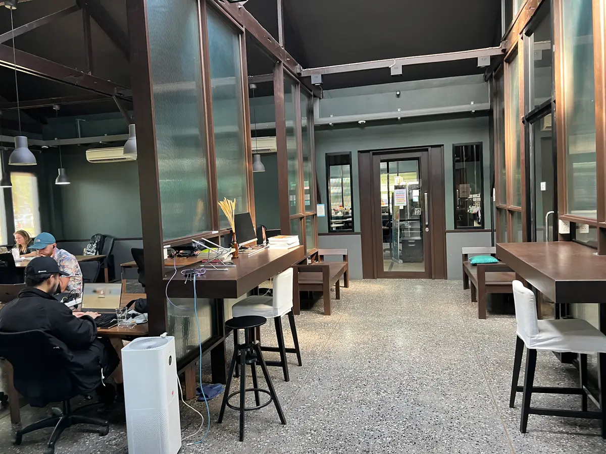 Long wooden desks and stools in a bright hall with a glass door and an air purifier.