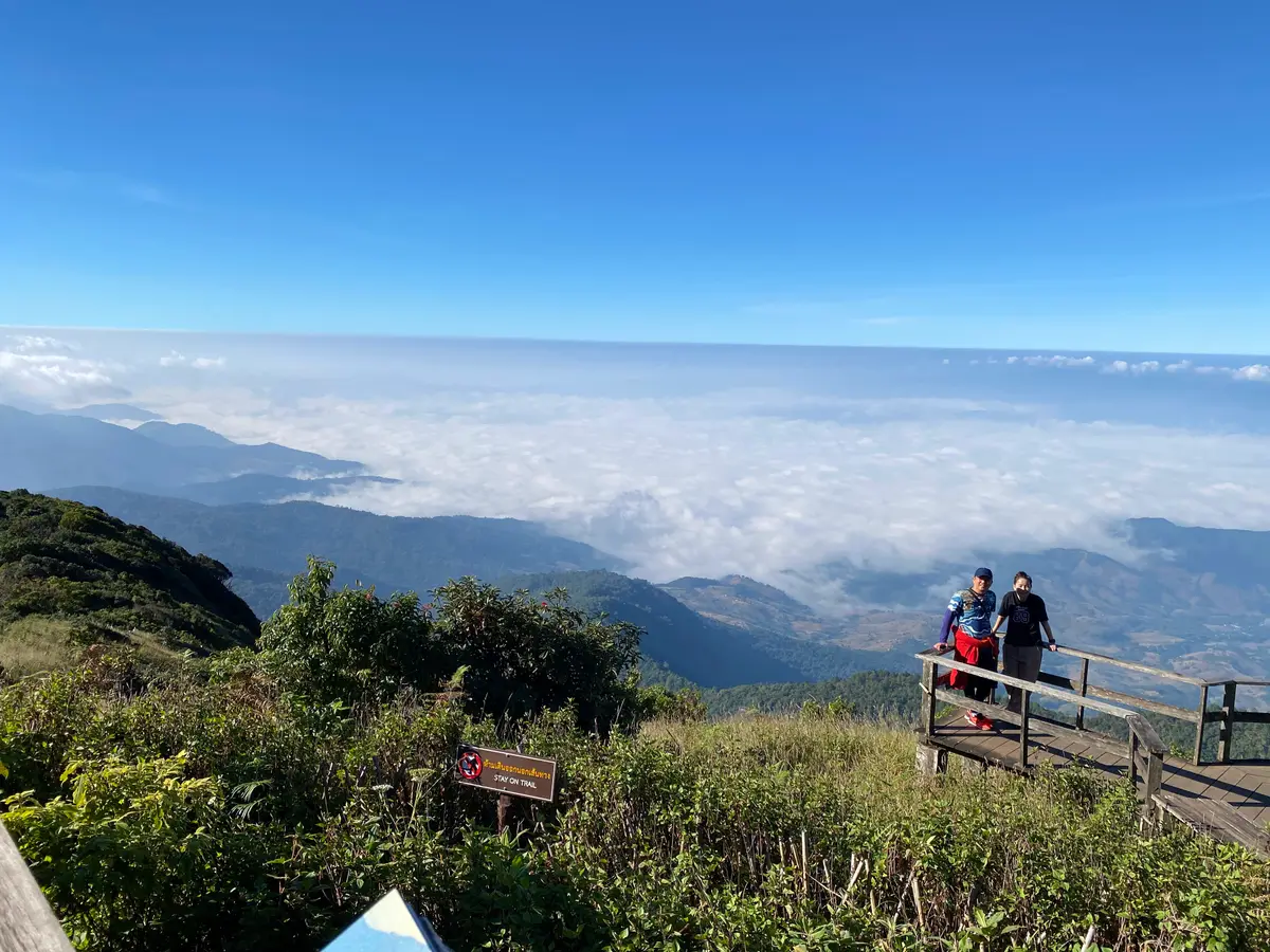 Sea of clouds below a mountain viewpoint with two visitors at a wooden railing