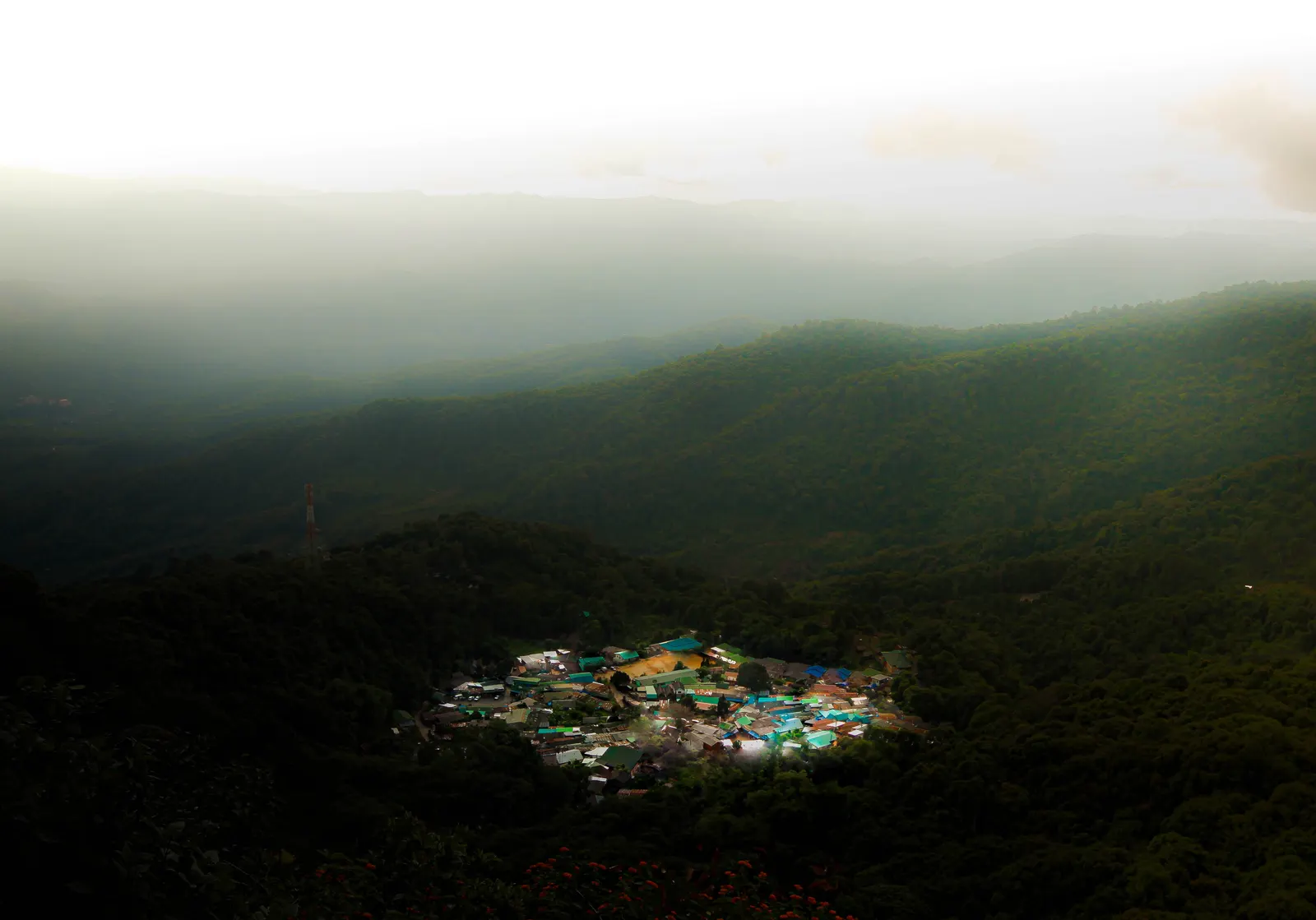 Aerial view of a small cluster of coloured village roofs in a misty forested valley