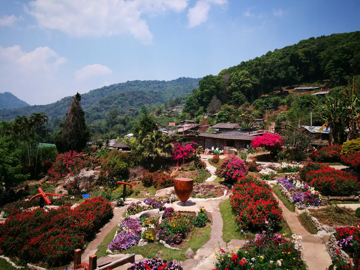 Flower garden with a large clay urn in front of village houses on a forested hillside