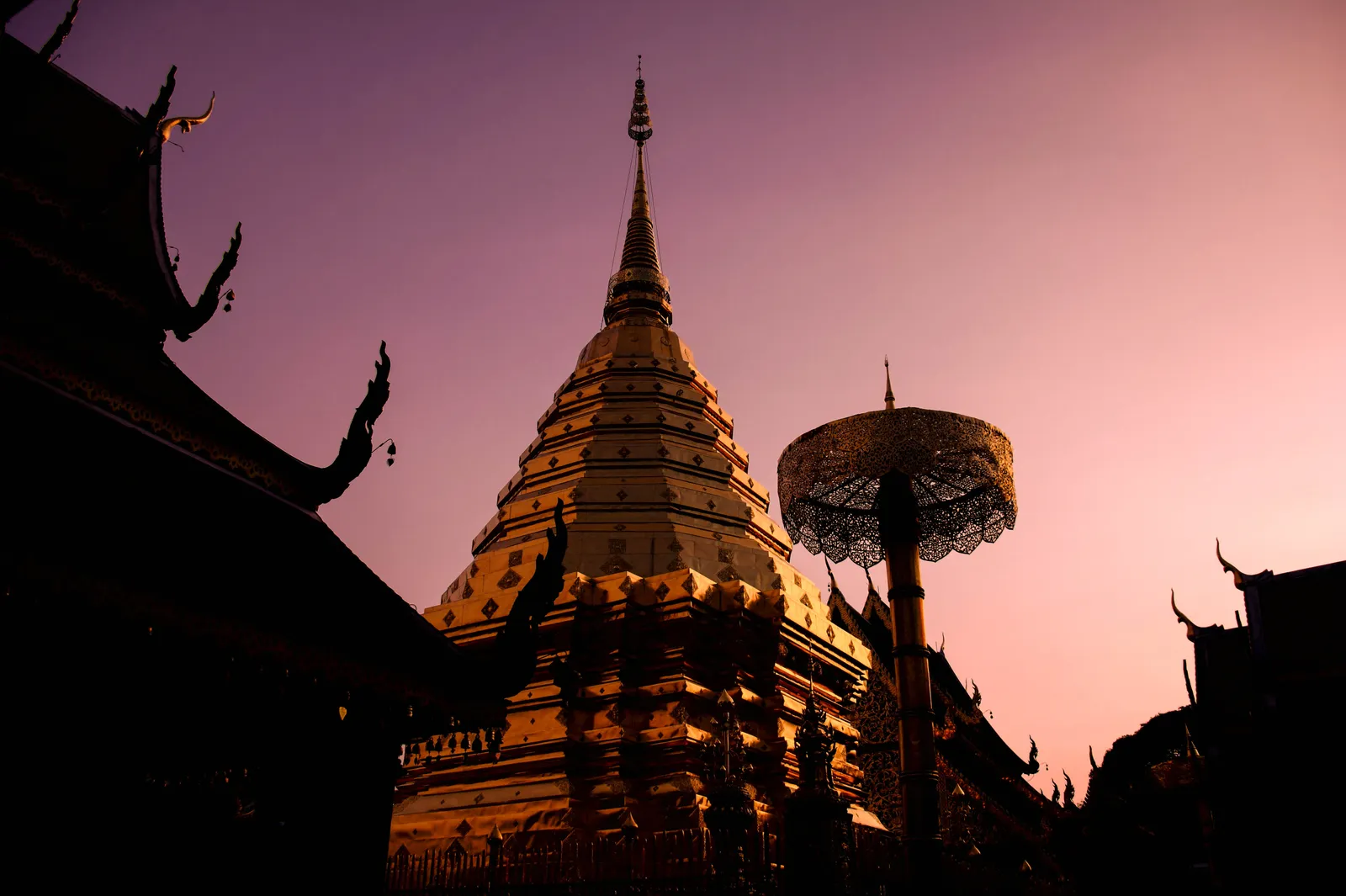 Gold chedi and a tall umbrella silhouetted against a pink dusk sky