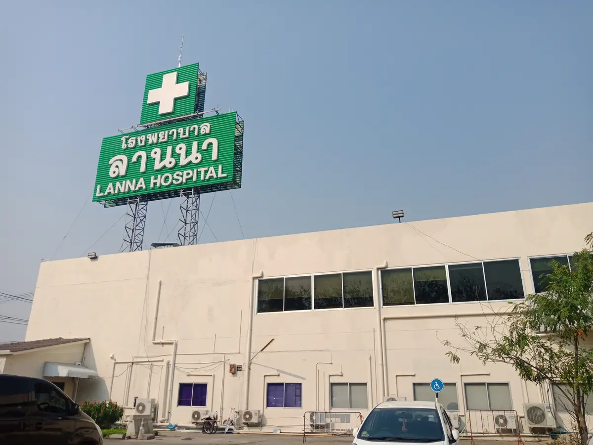 Green and white Lanna Hospital sign on the roof of a pale building.
