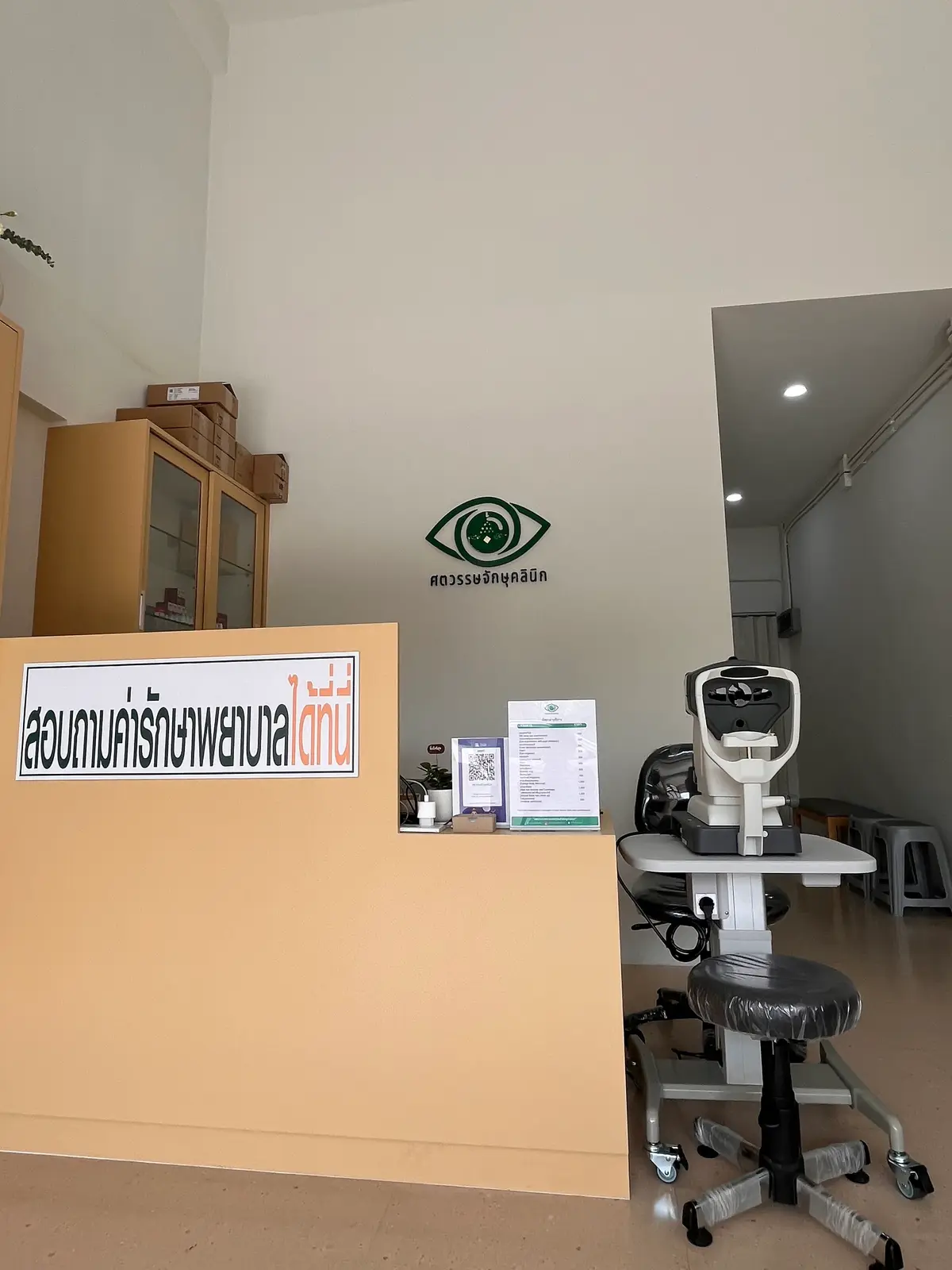 Reception desk with a green eye logo on the wall and an eye-test instrument on a side table
