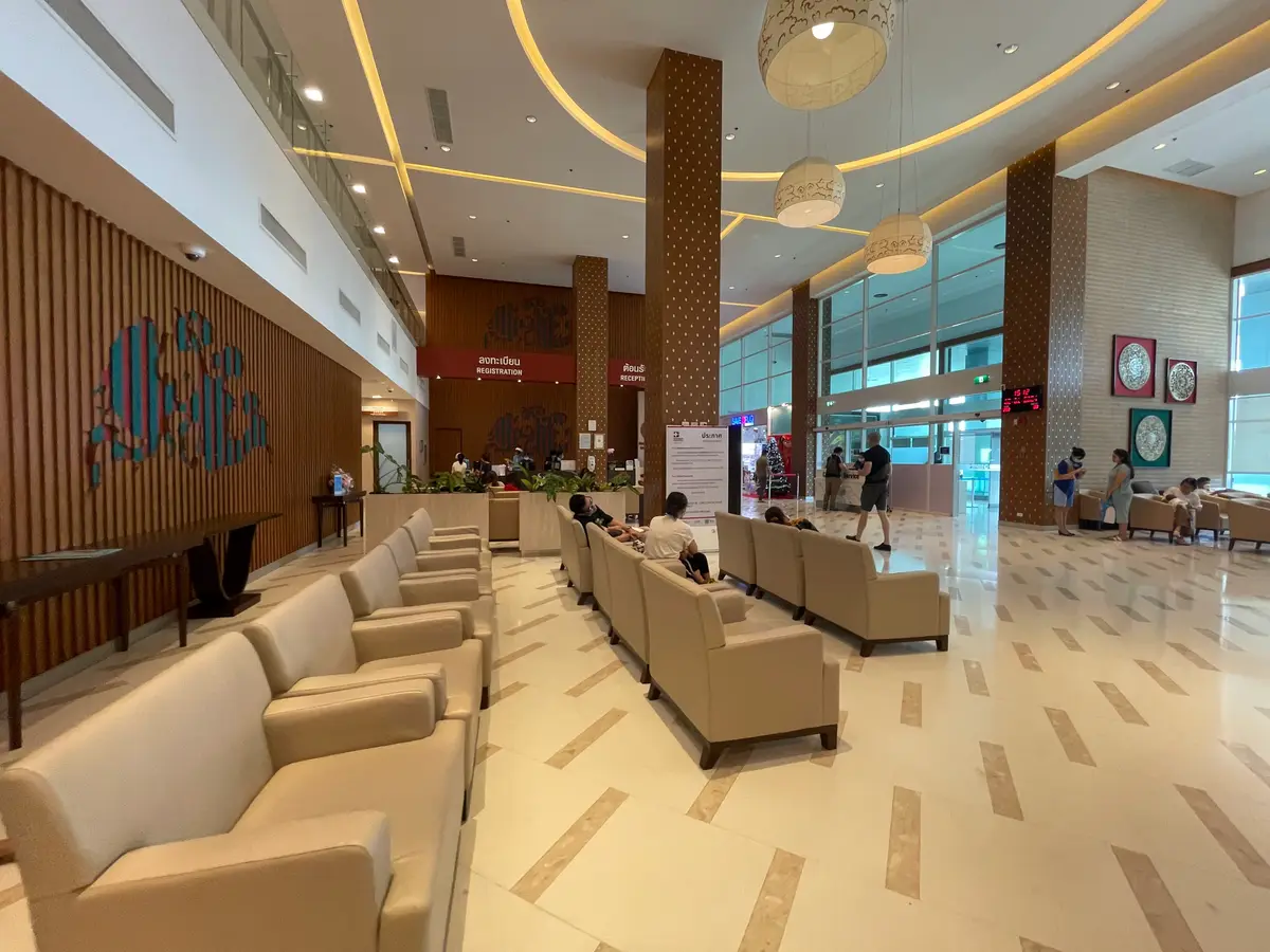 Wide hospital lobby with wooden wall panels, rows of cream sofas and people waiting