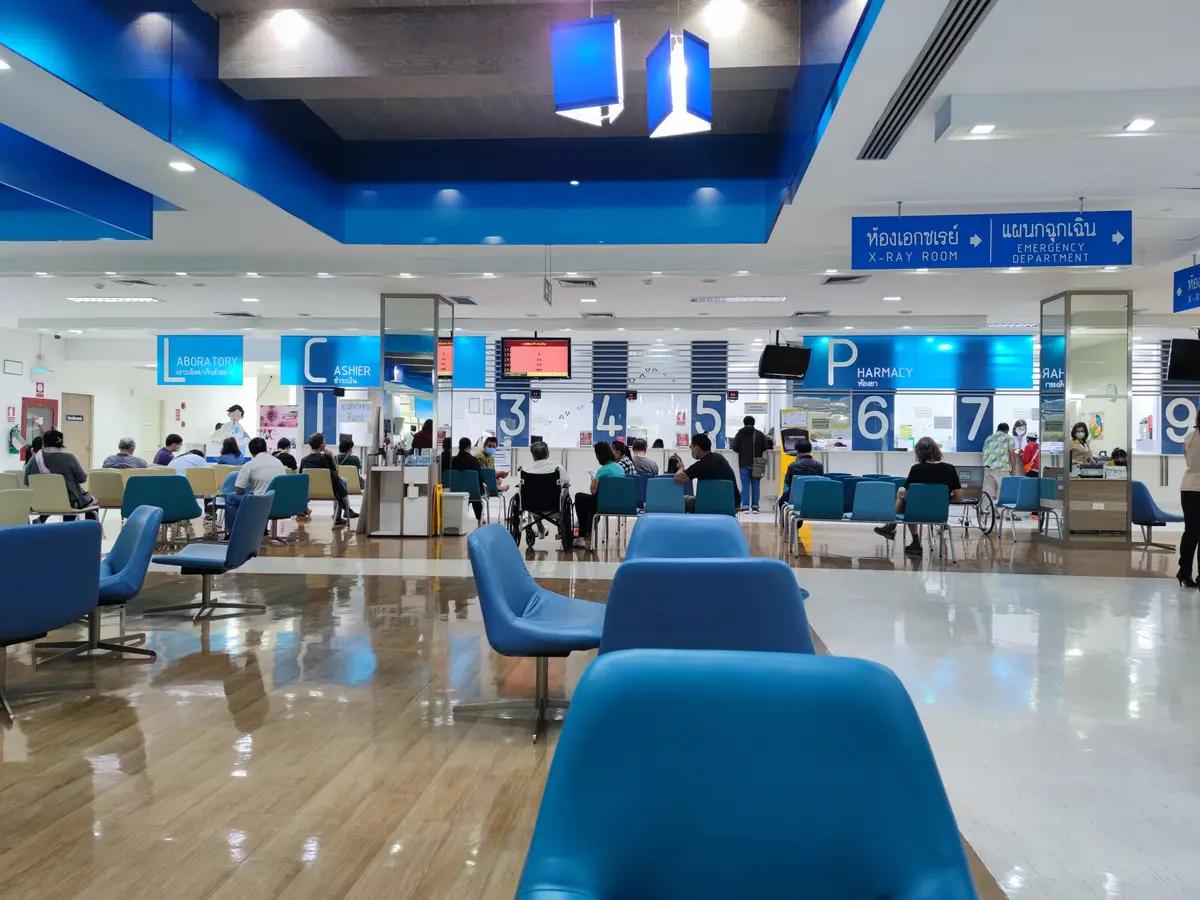 Large outpatient hall with blue chairs facing a row of numbered service counters