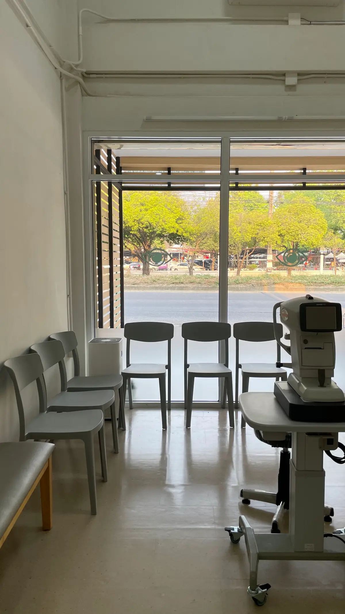 Grey waiting chairs in front of a window with an eye-examination machine on a table beside them