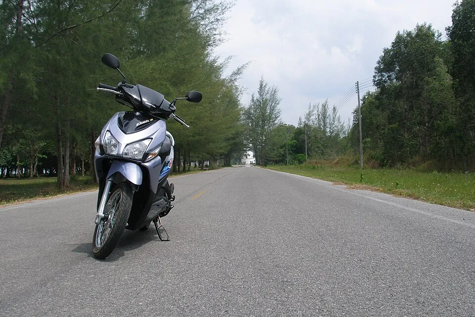 Silver and blue scooter parked on an empty road lined with pine trees