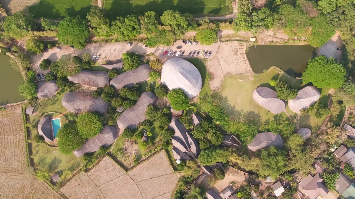 Aerial view of dome-shaped school buildings among trees, rice plots and a pond