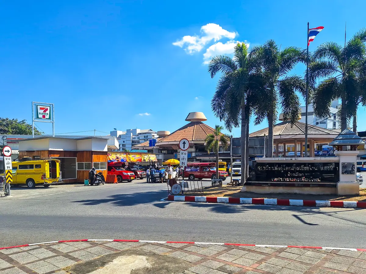 Bus terminal forecourt with yellow and red trucks parked beside a roundabout and palm trees