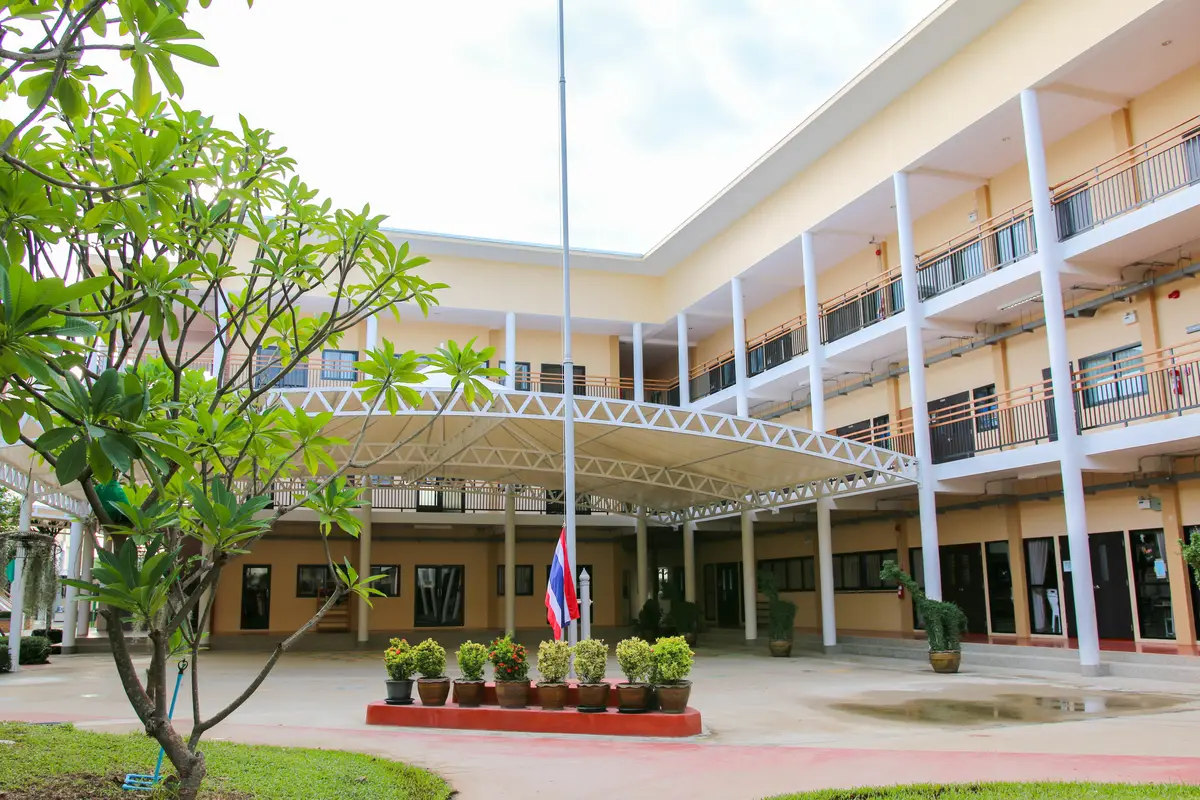 Two-storey school building with a covered walkway, a flagpole and potted plants in front