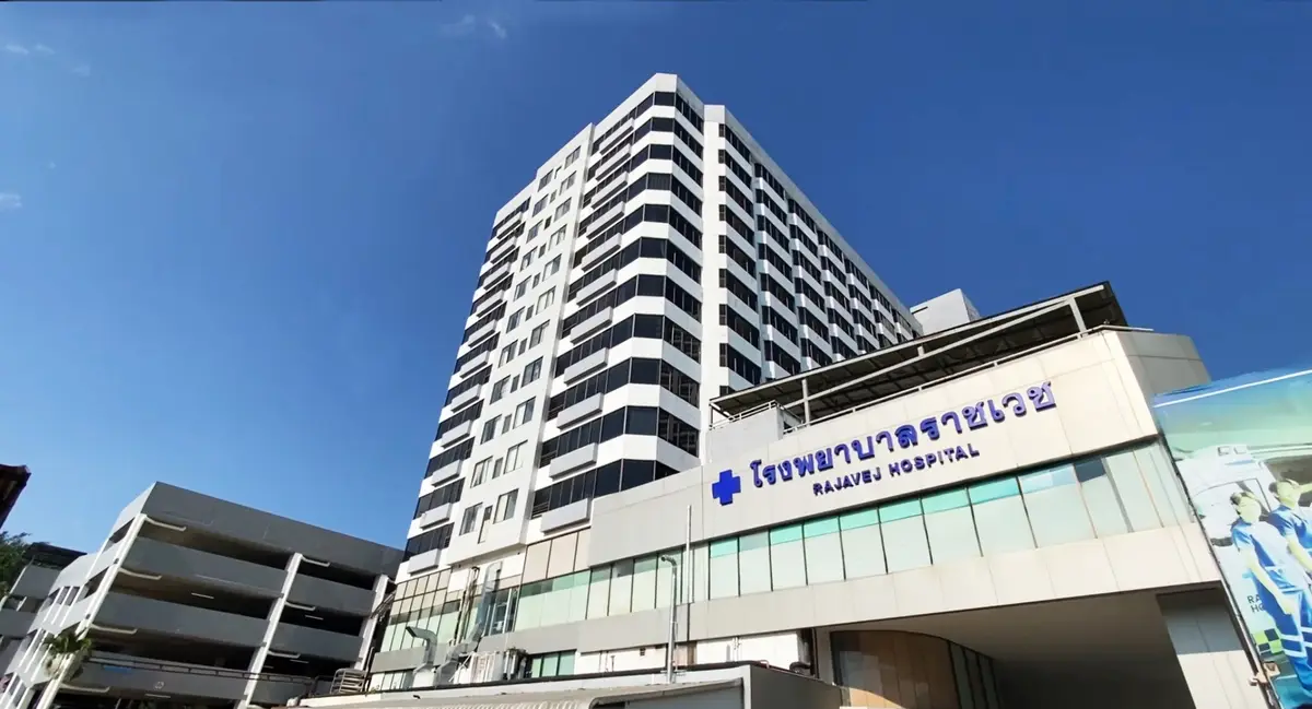 Tall white hospital tower with a blue cross and the words Rajavej Hospital against a blue sky.