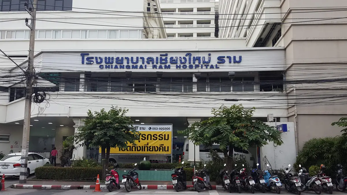 Front of Chiangmai Ram Hospital with a blue Thai and English sign above the entrance and a row of parked motorbikes.