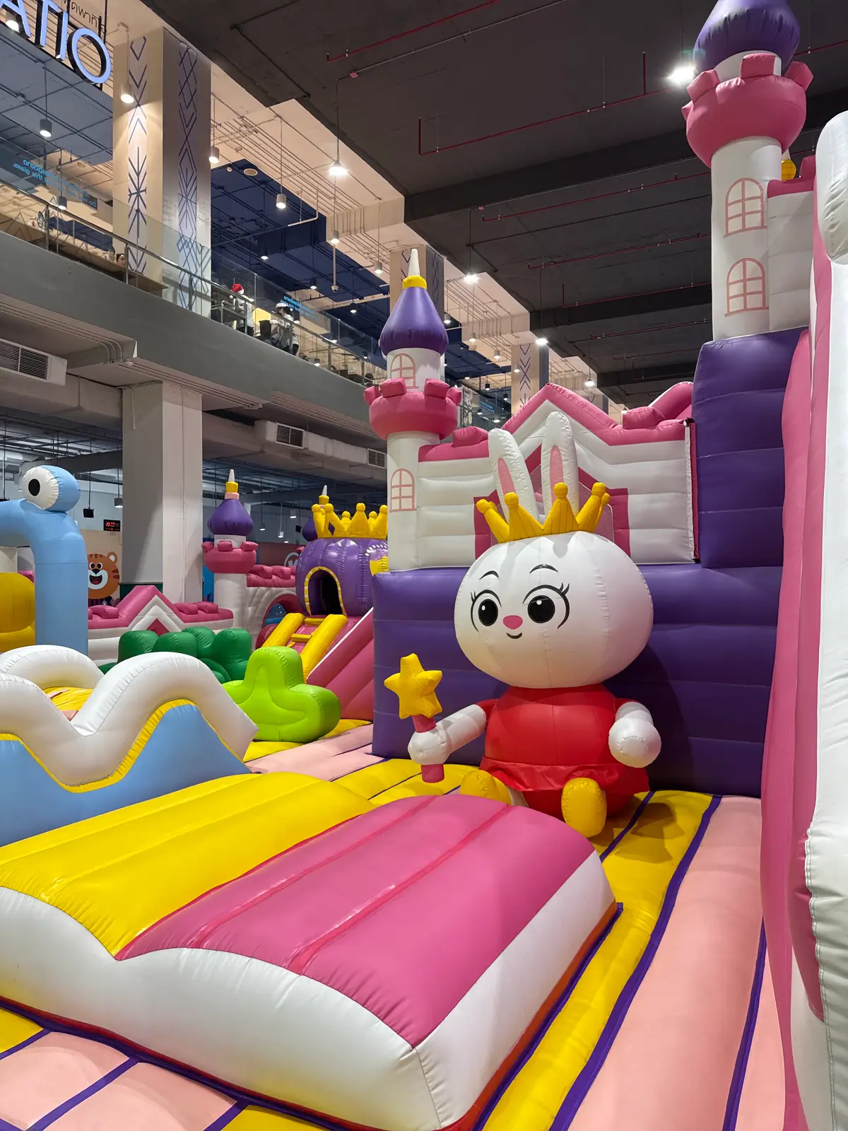 A white rabbit mascot figure beside a purple inflatable castle with slides in a large indoor hall.