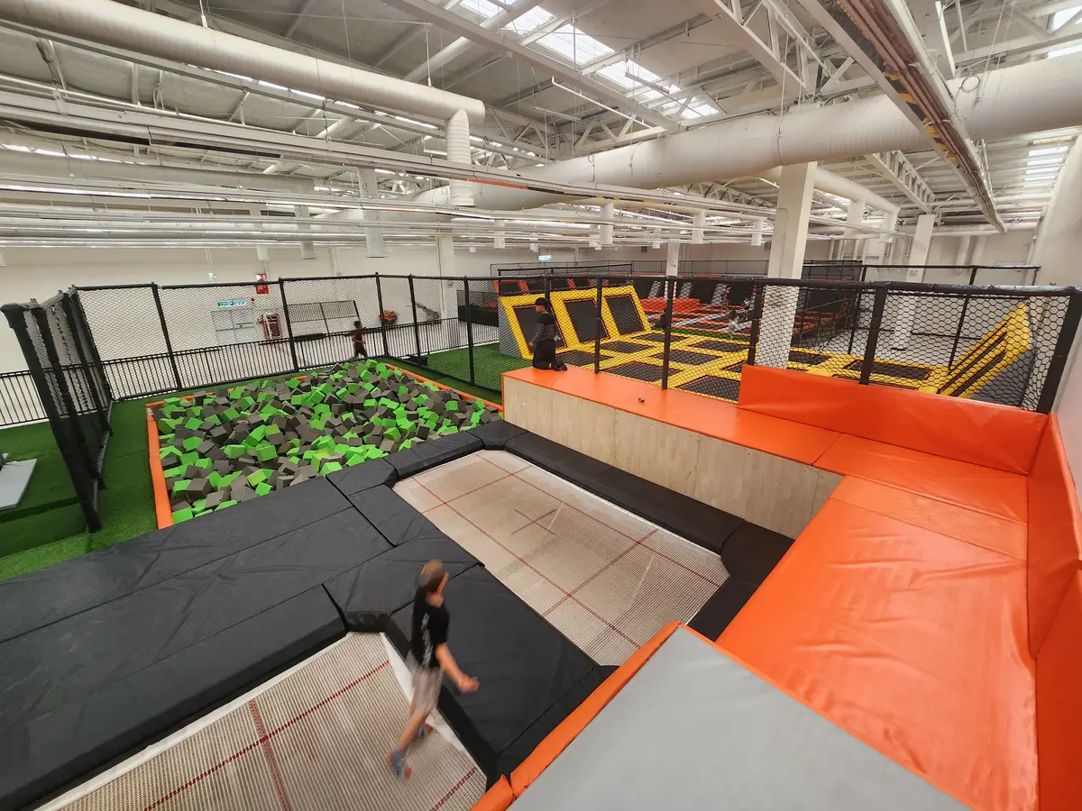 A wide trampoline hall with orange padded walls, angled trampoline ramps and a foam pit.