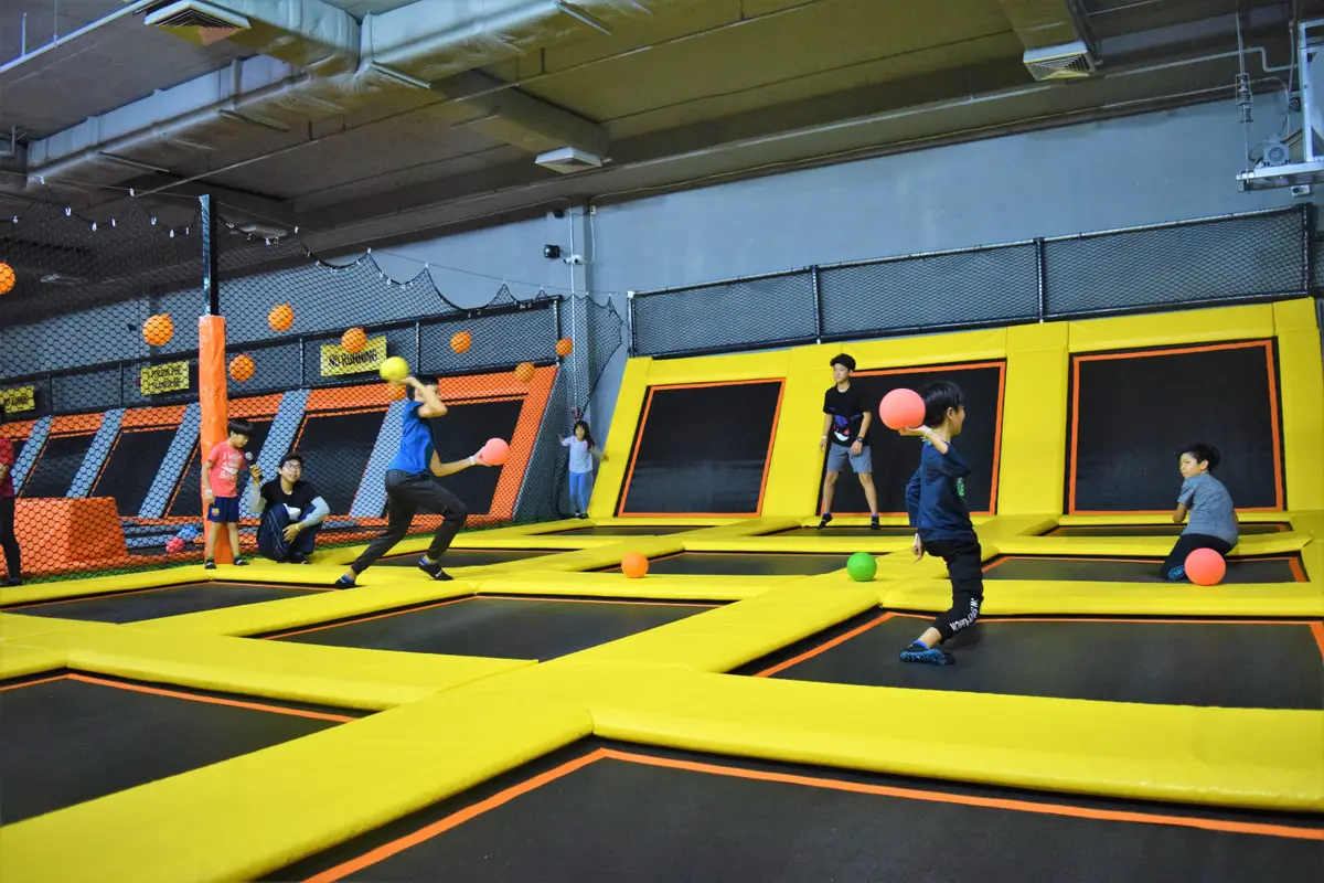 Children playing dodgeball on a yellow-edged trampoline court.