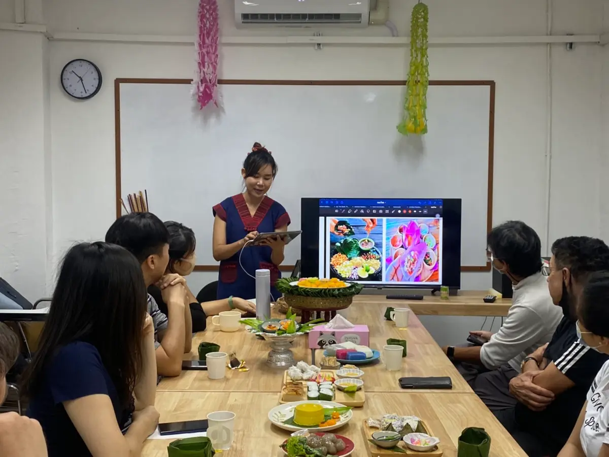 Teacher presenting a food photo slide to students seated around a table set with Thai dishes