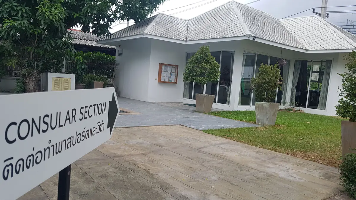 Direction sign reading Consular Section in front of a white single-storey building
