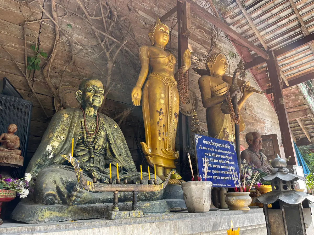 Gold standing and seated figures in a rustic wooden shelter with candles and incense