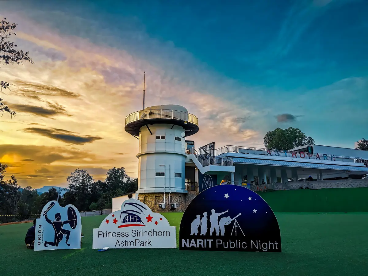 A white observatory tower on a lawn at sunset, with signs for Princess Sirindhorn AstroPark and NARIT Public Night in front.