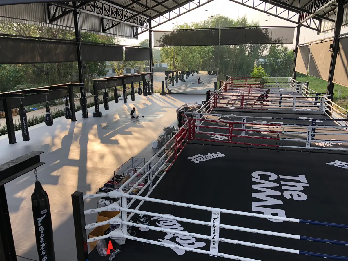 Boxing ring with white ropes and a black canvas reading The Camp, with training space beside it.