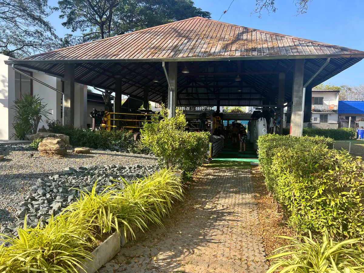 Open-sided roofed training hall at the end of a brick path lined with shrubs.