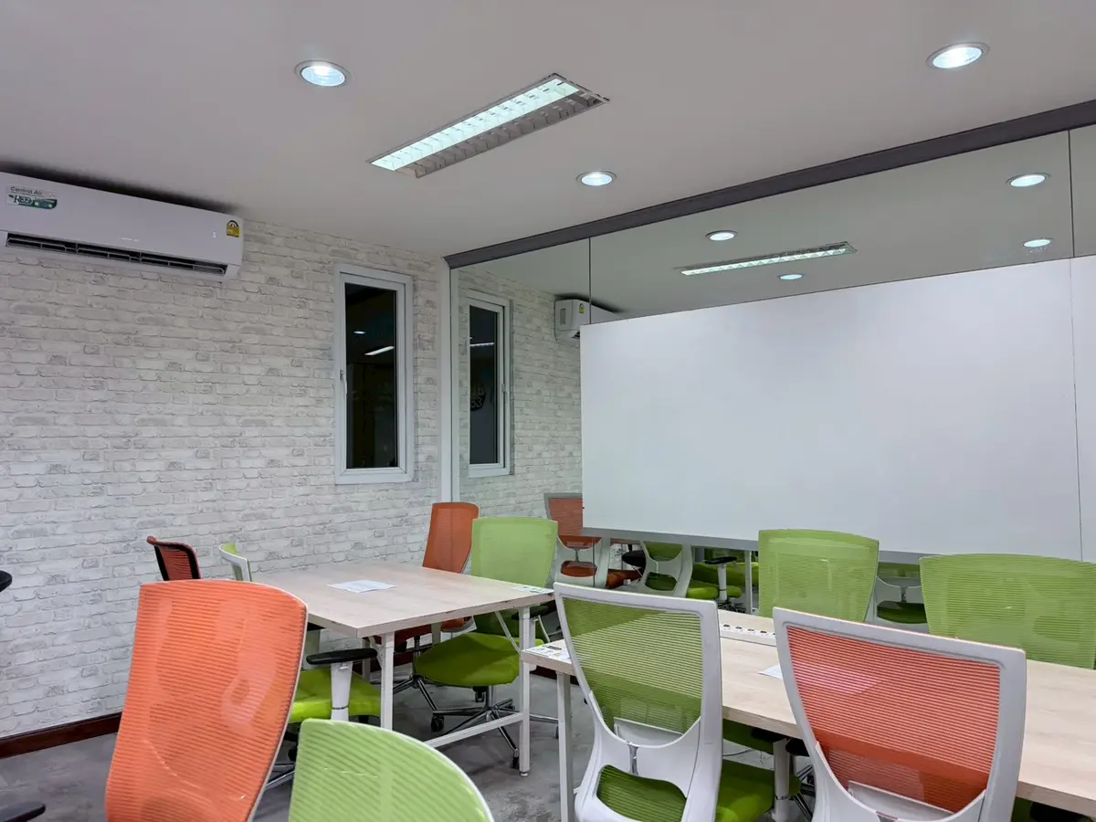 Meeting room with tables, orange and green chairs and a whiteboard wall