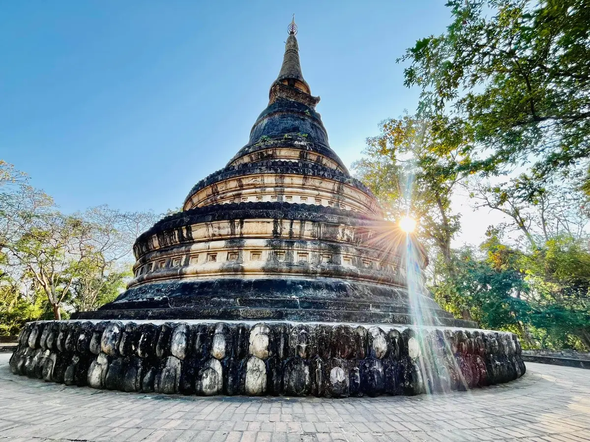 Bell-shaped dark chedi ringed at its base by weathered statue heads, with sun behind it