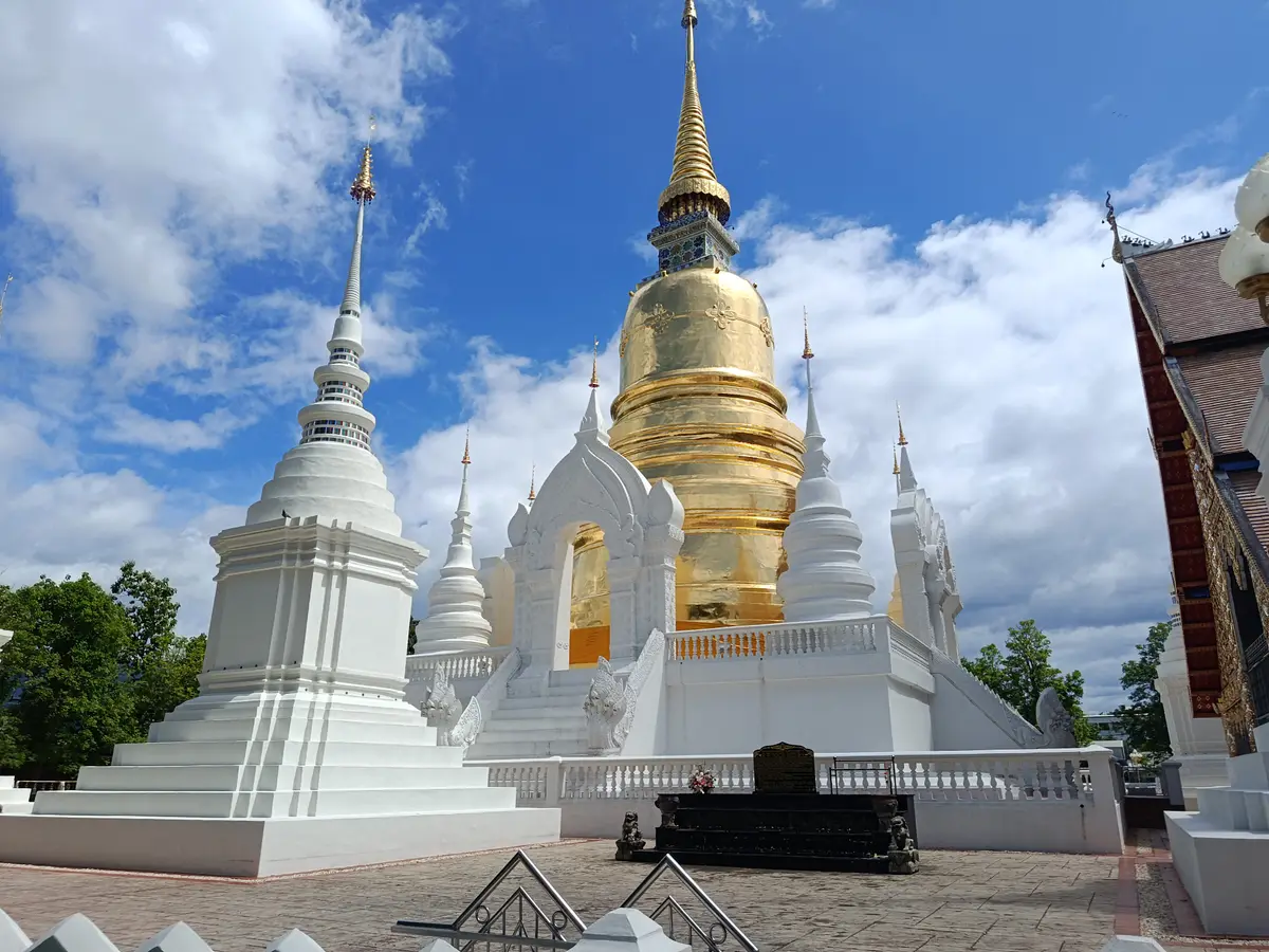White shrine chedis around a tall gold chedi under blue sky and clouds