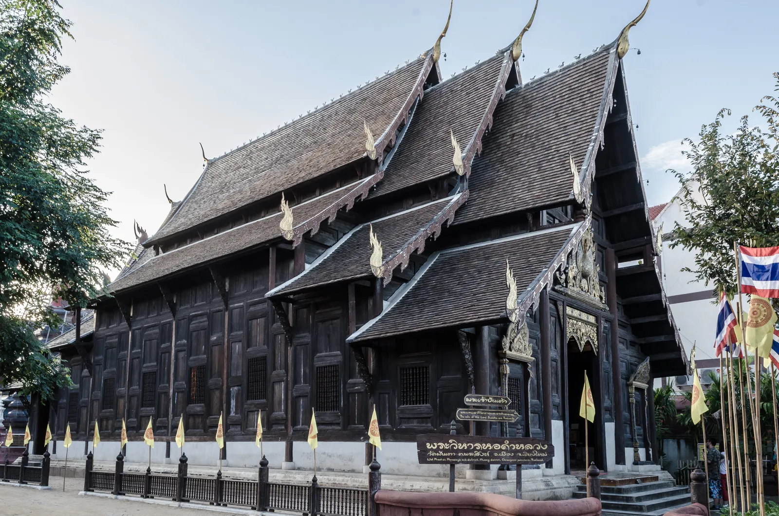 Dark teak hall with stacked steep tiled roofs and small yellow flags along its front