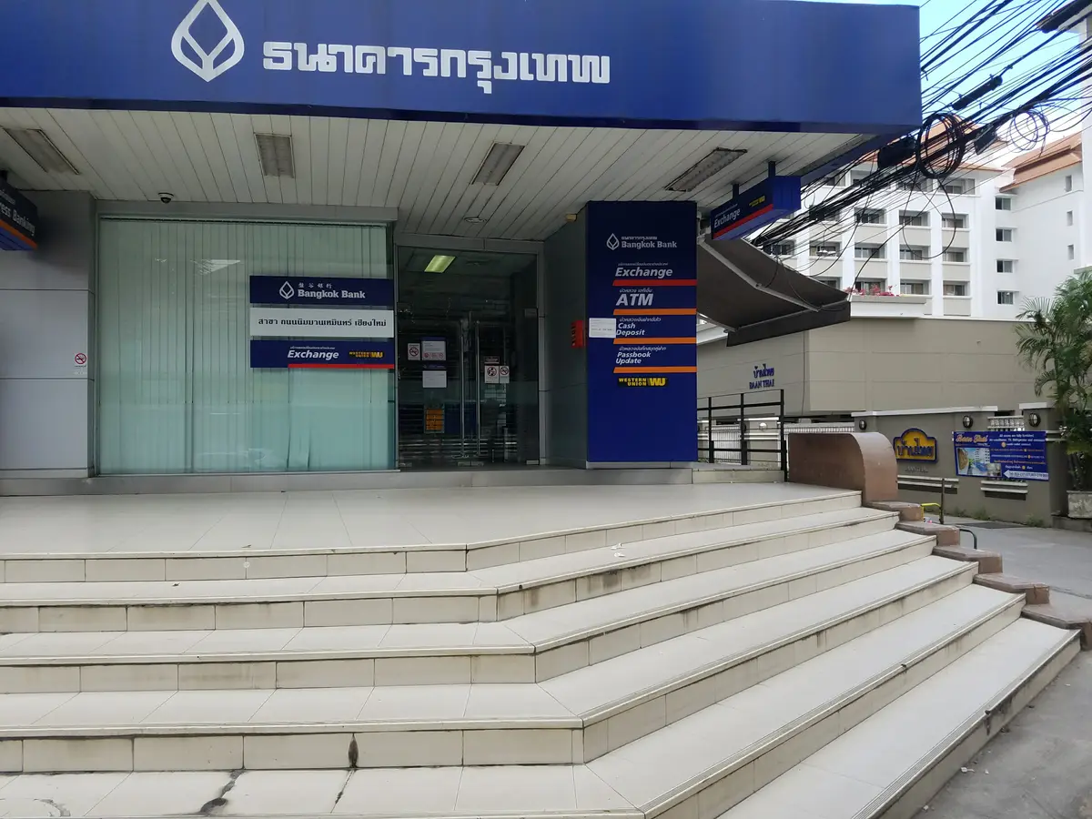 Bangkok Bank branch entrance with blue Exchange and ATM signs beside the glass doors above wide steps.