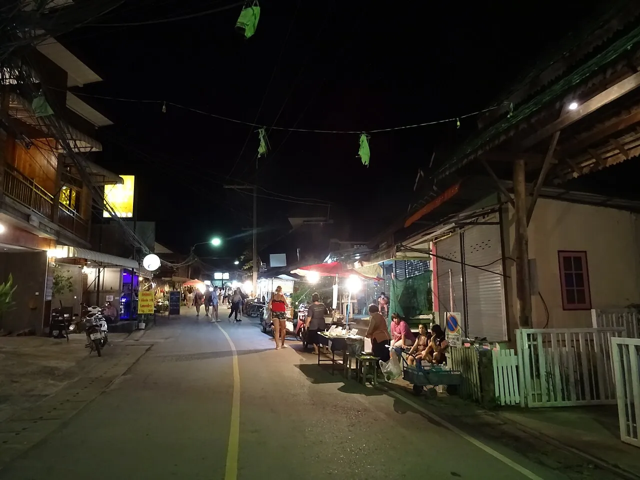 Night street with food stalls, shopfronts and walkers under street lights