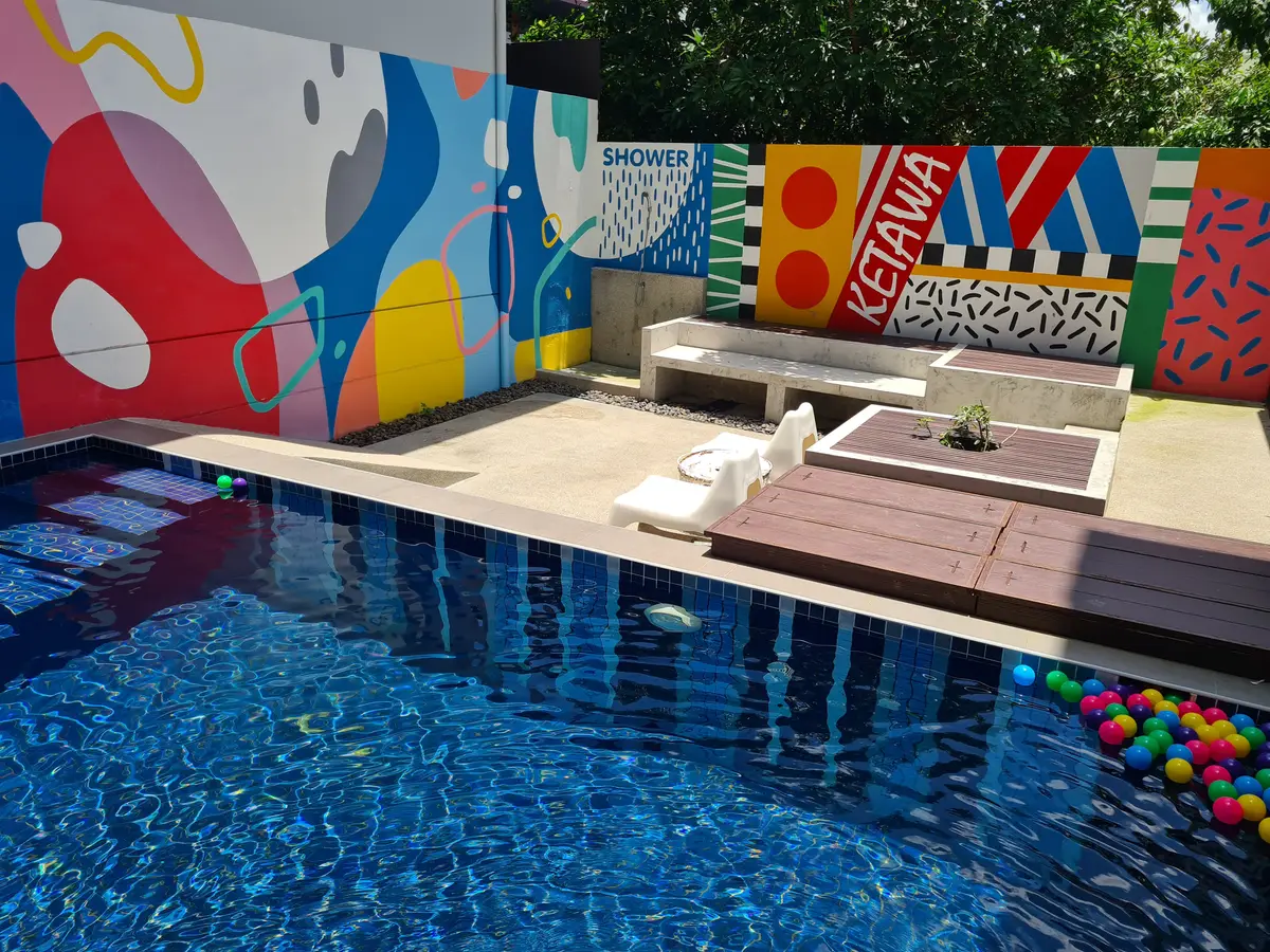 Swimming pool with a colourful painted wall and loungers beside it