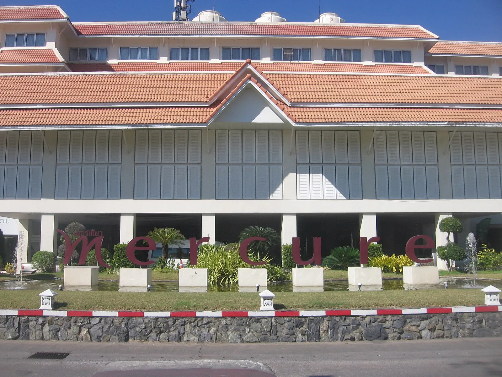 Hotel building with tiled roofs and large red lettering in a landscaped forecourt