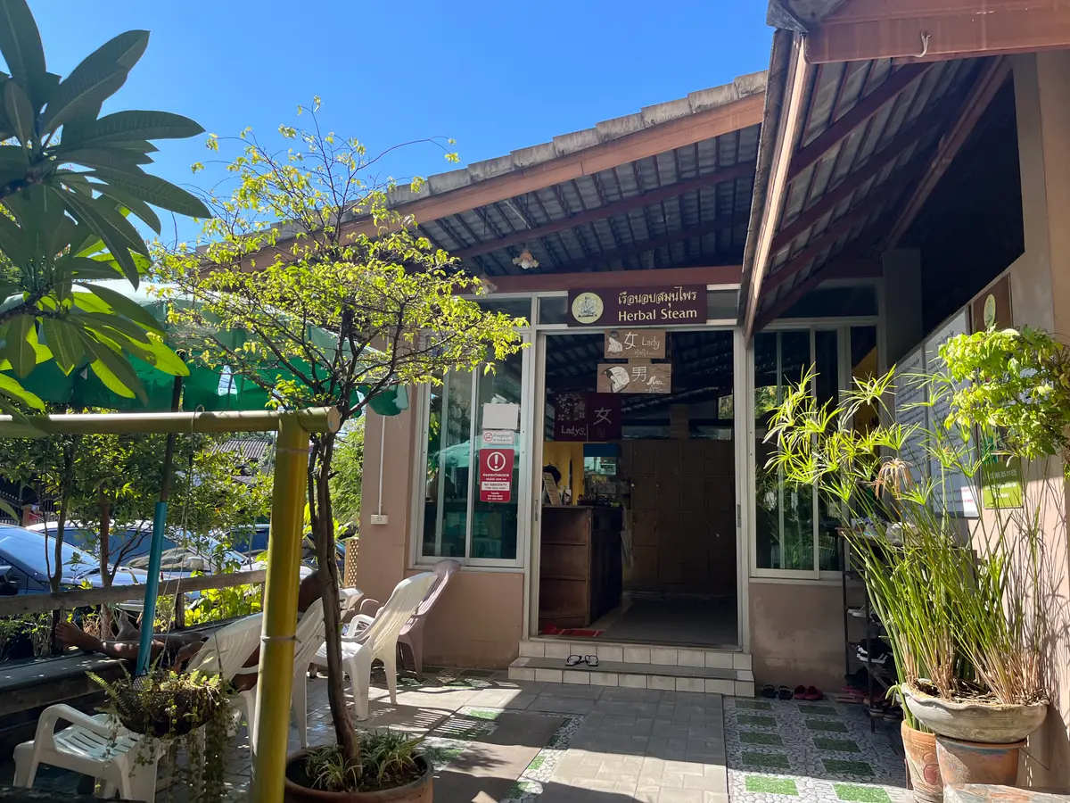 A shop entrance with potted plants and a covered terrace with white chairs.