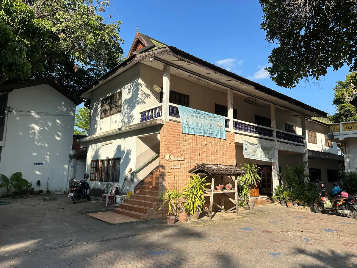 A white and brick two-storey building with a wooden balcony, motorbikes parked outside.